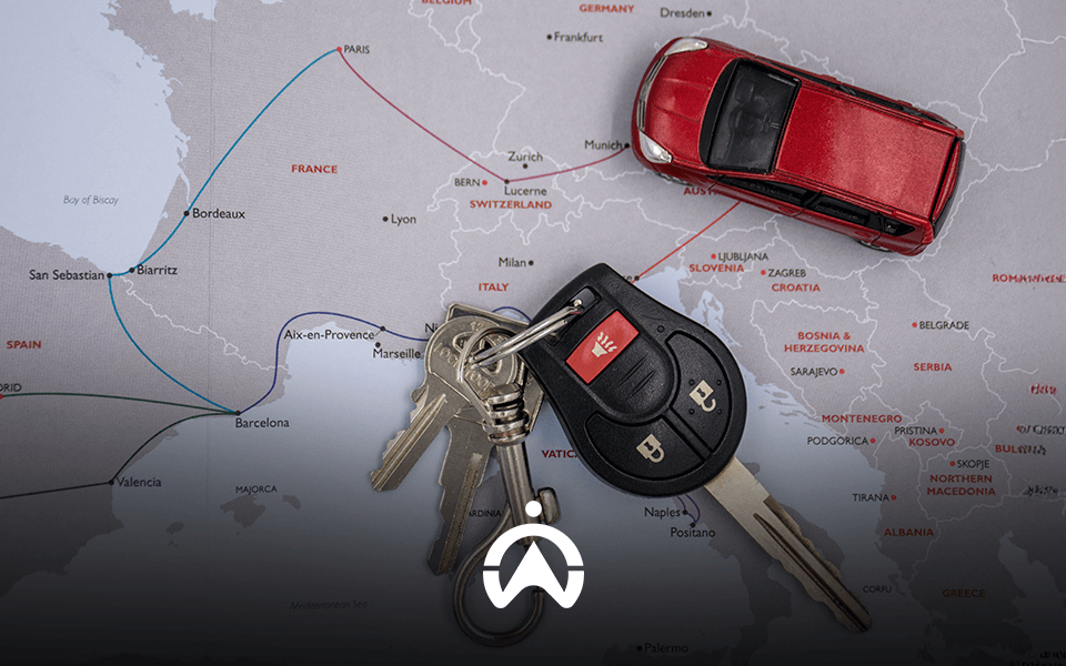 A red toy car and a set of keys placed on a map of Europe, highlighting travel routes in France, Spain, and beyond.