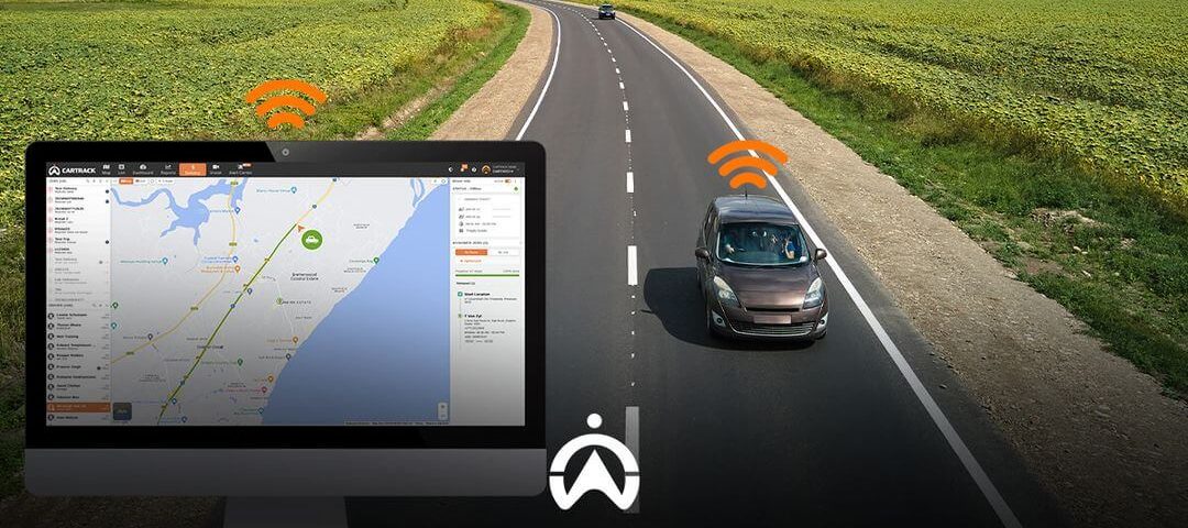 A computer screen displays a map with a tracking interface, while a car drives along a rural road nearby, indicating GPS connectivity.