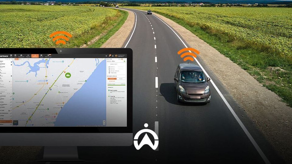 A computer screen displays a map with a tracking interface, while a car drives along a rural road nearby, indicating GPS connectivity.